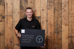 Nick Salini, Director of Thermal Earth Ltd, holding a 'Proud to be an MCS certified heat pump contractor' sign.